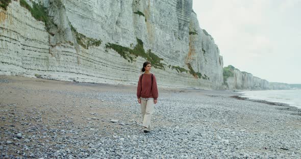 A Young Woman Walks Along a Pebbly Beach Past Sheer Chalk Cliffs