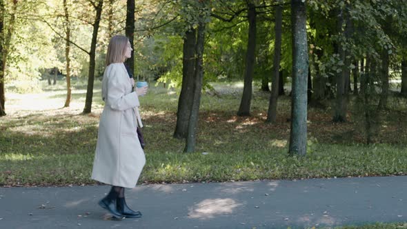 Young Girl Walks in the City Park on a Sunny Autumn Day Wearing a Coat