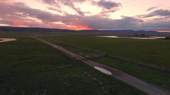 Flying alongside dirt road during colorful sunset in Star Valley Wyoming