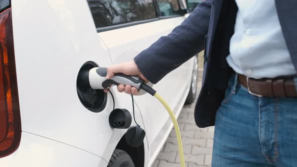 Man Coming to the Electric Car and Plugging in a Charging Cable