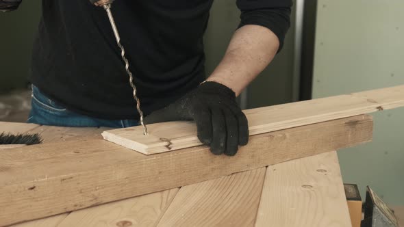 A Male Construction Worker Uses a Drill to Make a Hole in a Wooden Plank