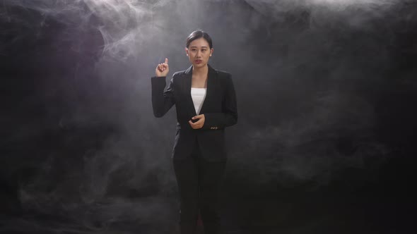 Asian Speaker Woman In Business Suit Holding Her Hands Together While Speaking In The Black Studio