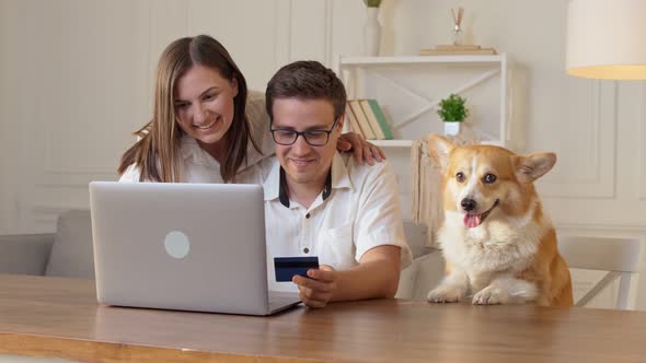 Cheerful Young Couple With a Dog Shopping Online While Sitting Home.