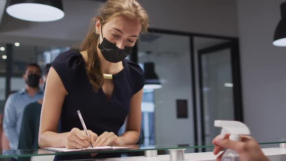 Caucasian woman in face mask has hands disinfected by male colleague at office reception desk