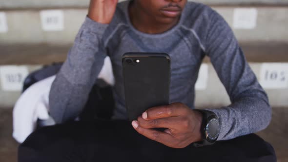 Disabled mixed race man with prosthetic legs sitting on a stadium and using a smartphone