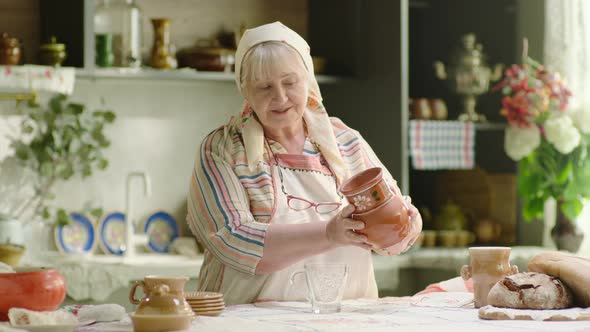 Grandmother Pouring Milk Into the Glass From Crock in the Country