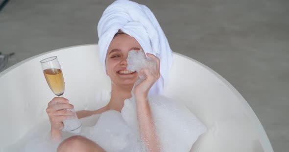 Closeup Portrait of Attractive Sexy Woman Lying Naked in Bathtub Full of Foam in Modern White