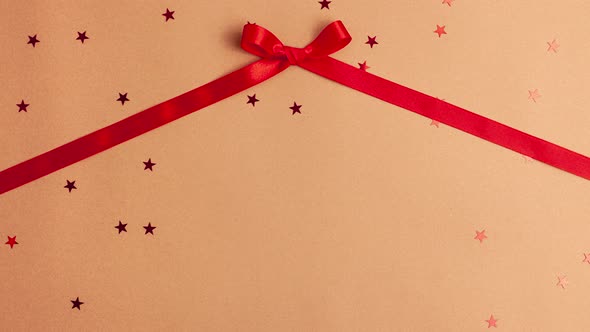 Red satin ribbon bow that tied and untied on brown background with red stars shapes