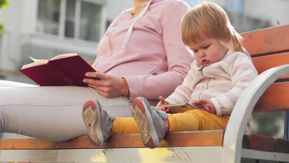 Mother and her little child sitting on a bench and relaxing with book and smartphone. Bottom view.