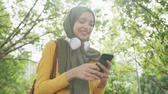 Woman wearing hijab with wireless headphone and using her phone