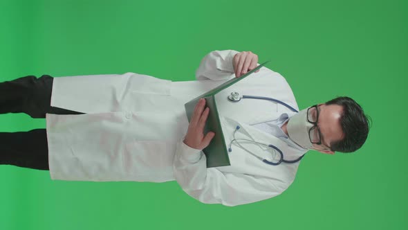 Asian Doctor With Stethoscope Wearing Mask, Reading Document While Walking On Green Screen