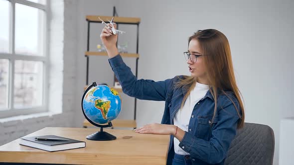 Young Exciting Woman Moving Toy Plane Around the Globe.