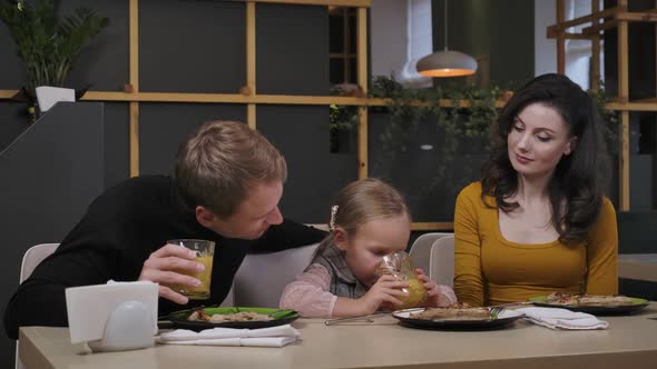 Happy Couple of Parents Admiring Cute Charming Daughter Drinking Orange Juice and Talking