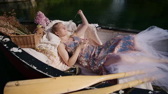 Woman daydreaming on sunny day laying down in a traditional rowboat, static shot