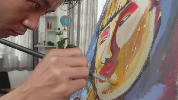 Close Up Of An Asian Artist Man Holding Paintbrush And Painting A Girl's Face On The Canvas