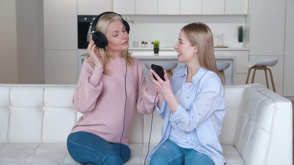 Smiling Adult Daughter and Senior Mother Listening To Music on Headphones Together Enjoying Family