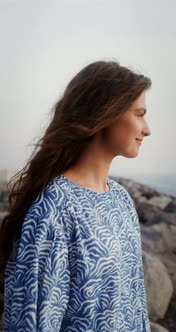 A Woman Stands on Large Stones on the Seashore and Smiles Looking Into Distance