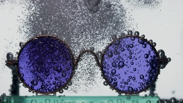 A Stream of Soda is Poured Into the Water Over Stylish Round Sunglasses Creating a Whirlwind of
