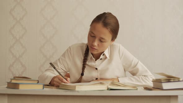 Young woman sits at desk, turns pages and writes out text from book. Education, studyings. Bookworm