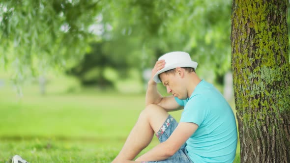 Man Is Sad While Sitting Under a Tree in a City Park Blurred Background