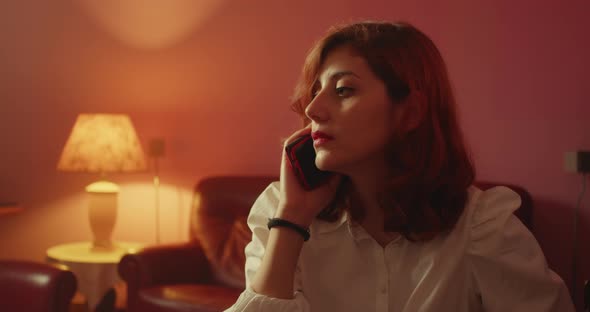 Girl with white shirt talking on the phone sitting on the sofa at home