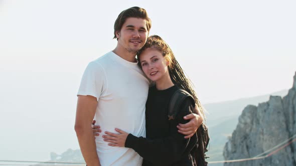 Young Cute Couple of Hikers Standing on a Background of Mountains and Looking in the Camera