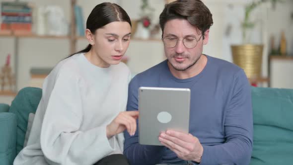 Hispanic Couple Using Tablet While Sitting on Sofa