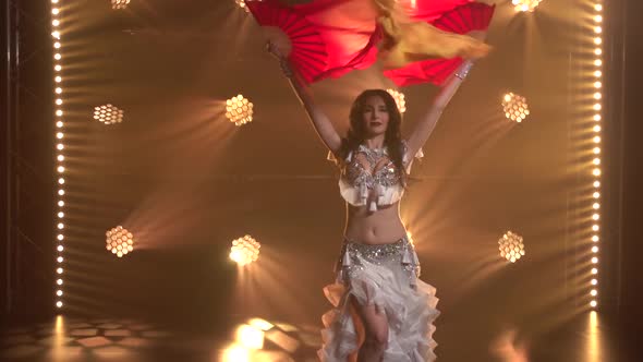 Female Belly Dancer in a White Oriental Costume Dancing Silk Fan Tissues. Shot in a Dark Studio with