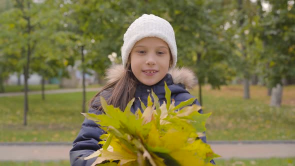 Portrait of a Caucasian Girl in White Hat Holding a Bunch of Yellow Leaves and Smiling