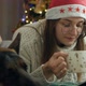 A Woman Lies on the Couch Near the New Year Tree and Looks at the Phone Screen Drinks Coffee - VideoHive Item for Sale