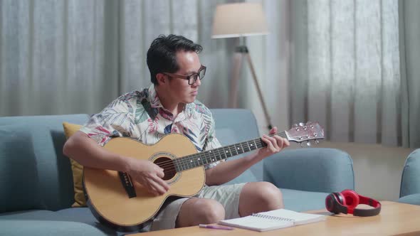 Asian Man Composer With Notebook On Table Playing Guitar At Home
