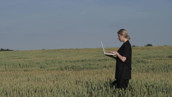 employee of an agricultural firm with a laptop checks the quality of wheat in the field