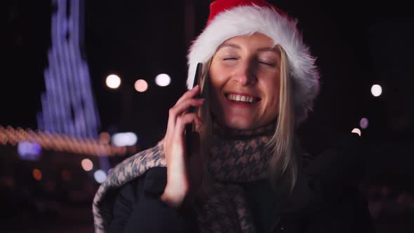 a woman chatting on her smartphone wearing a Santa hat is a night city.