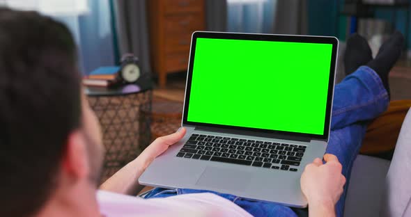 Young Man at Home Uses Green Mockup Screen Laptop