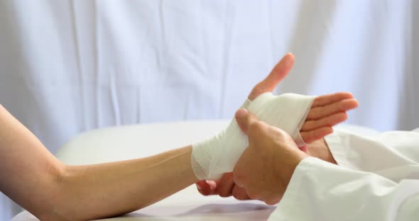 Physiotherapist putting bandage on injured hand of patient