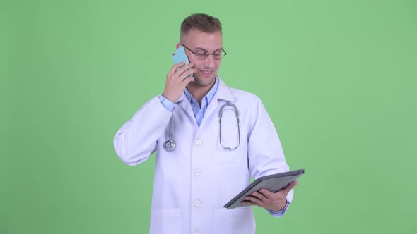 Happy Handsome Man Doctor Talking on the Phone While Using Digital Tablet