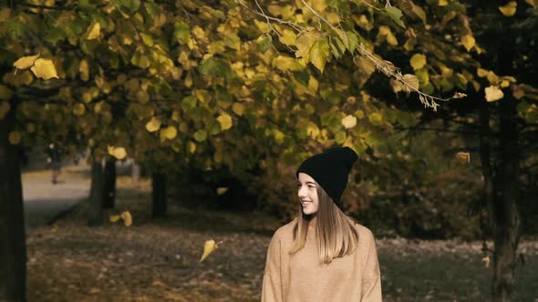 Happy Girl Smiling at Camera Under Falling Autumn Leaves in Park