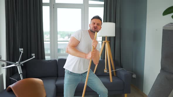 Man Cleaning the House and Having Fun Dancing and Singing with a Broom