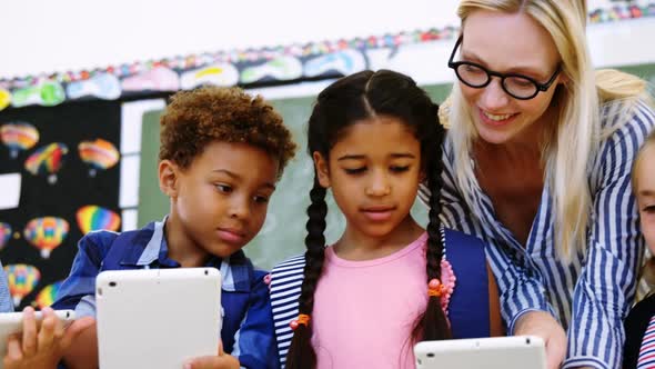 Teacher assisting schoolkid on digital tablet in classroom