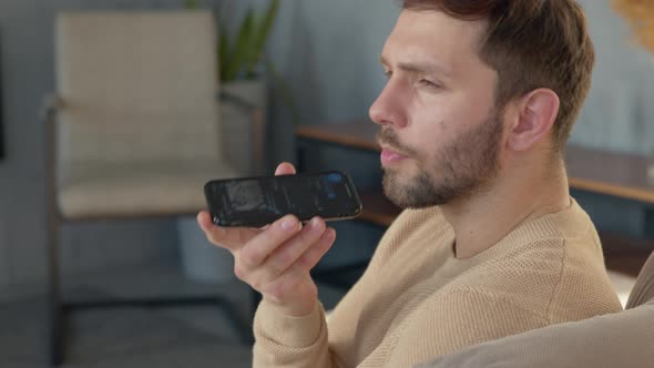 Man sitting on sofa holds phone talks on speakerphone