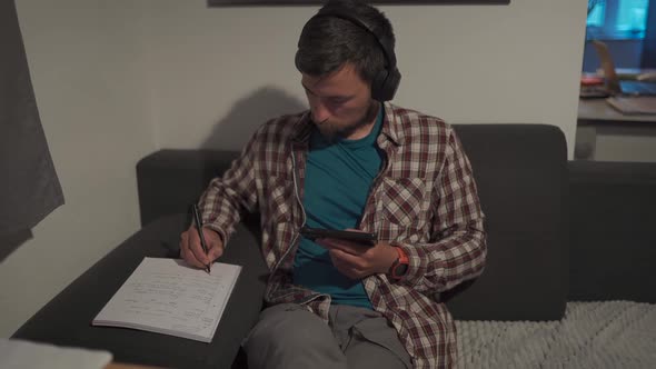 Student Uses Smart Phone and Earphones at Home While Studying Remotely Online Making Notes in