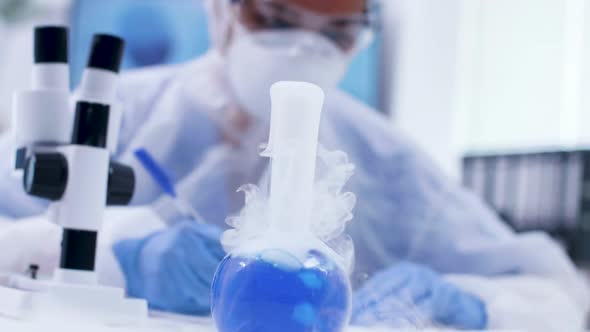 Handheld Footage of Smoking Blue Fluid Win Reagent and Scientist Looking Through Microscope alt