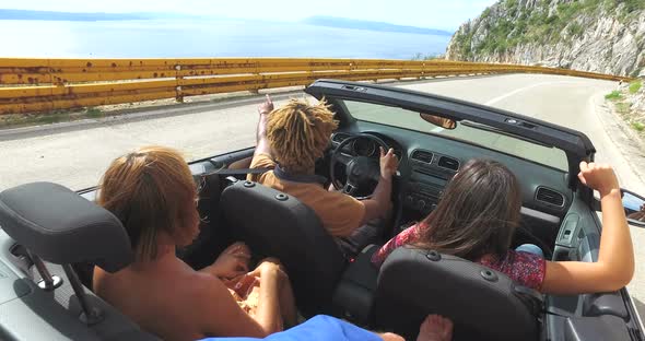 Friends having fun driving on the road along the coast in red convertible