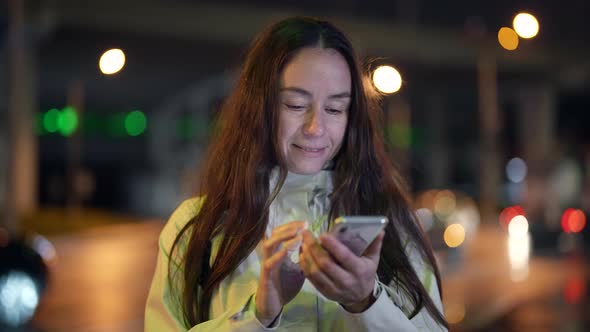 Portrait of a Brunette with Long Hair in the Evening Against the Background of Blurred City Lights