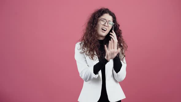 Agitated Young Woman with Curly Hair Talking on the Phone with Contempt Gesturing with Her Hand