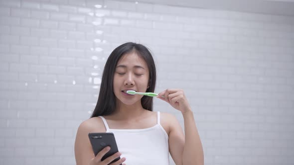 Daily routine concept. Asian girls playing mobile while brushing teeth. 4k Resolution.