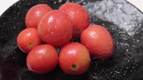 Small tomatoes in a dark dish being sanitized with water.