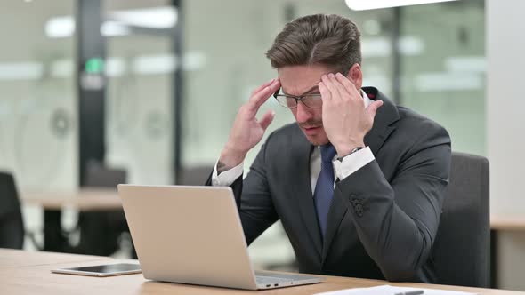 Stressed Middle Aged Businessman with Laptop Having Headache in Office 