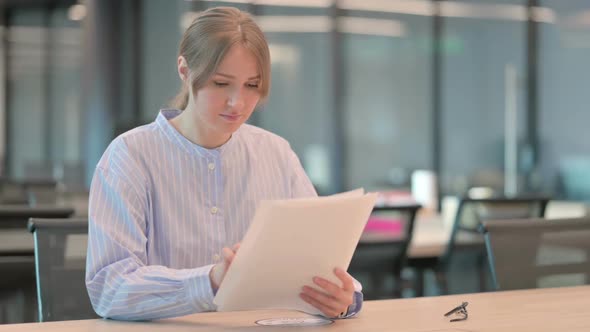 Young Woman Reading Reports While Sitting in Office