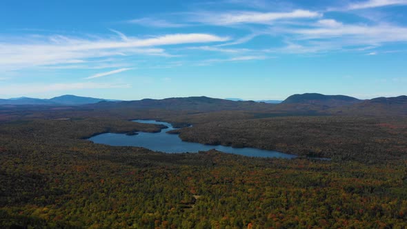 Aerial drone establishing shot over a calm blue forest lake with the thick green and autumn colored